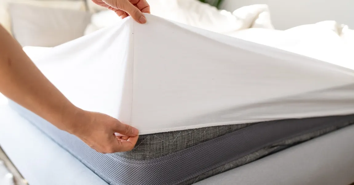 A person pulling a clean white fitted sheet over a mattress corner as a simple bed bug prevention measure.