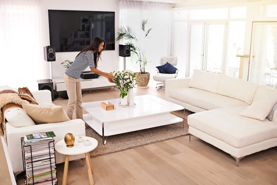 A woman decluttering and tidying up a bright modern living room to prepare her home for professional bed bug treatment.