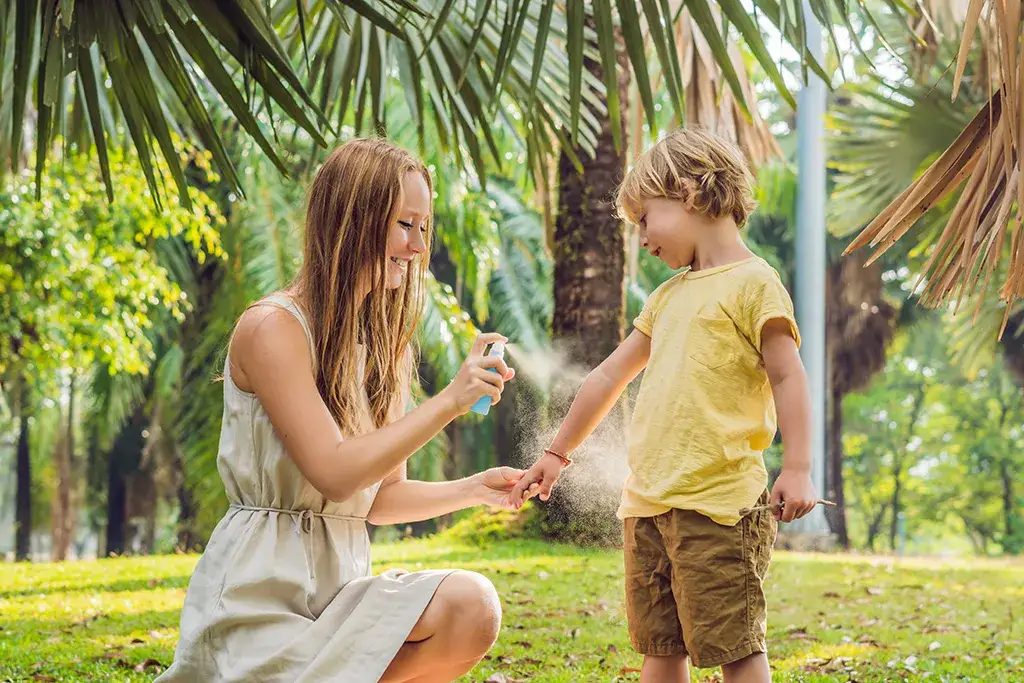 Mother applying mosquito repellent spray to her child outdoors