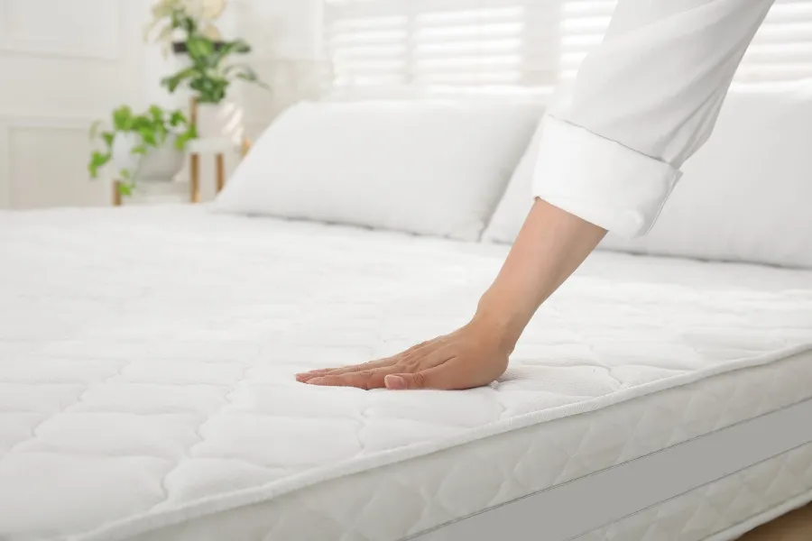 A person's hand smoothing down a clean, bare white mattress with a quilted cover after taking steps to get rid of bed bugs.