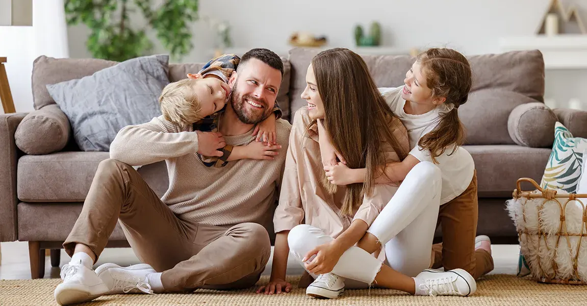 A happy family smiling and relaxing together on their living room floor, representing a safe, pest-free home for our rodent learning center.