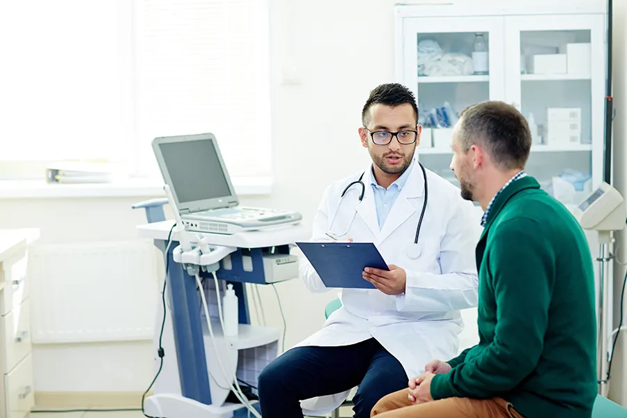 A male doctor holding a clipboard while consulting with a patient in an exam room, relevant to discussions about what diseases do rats carry.
