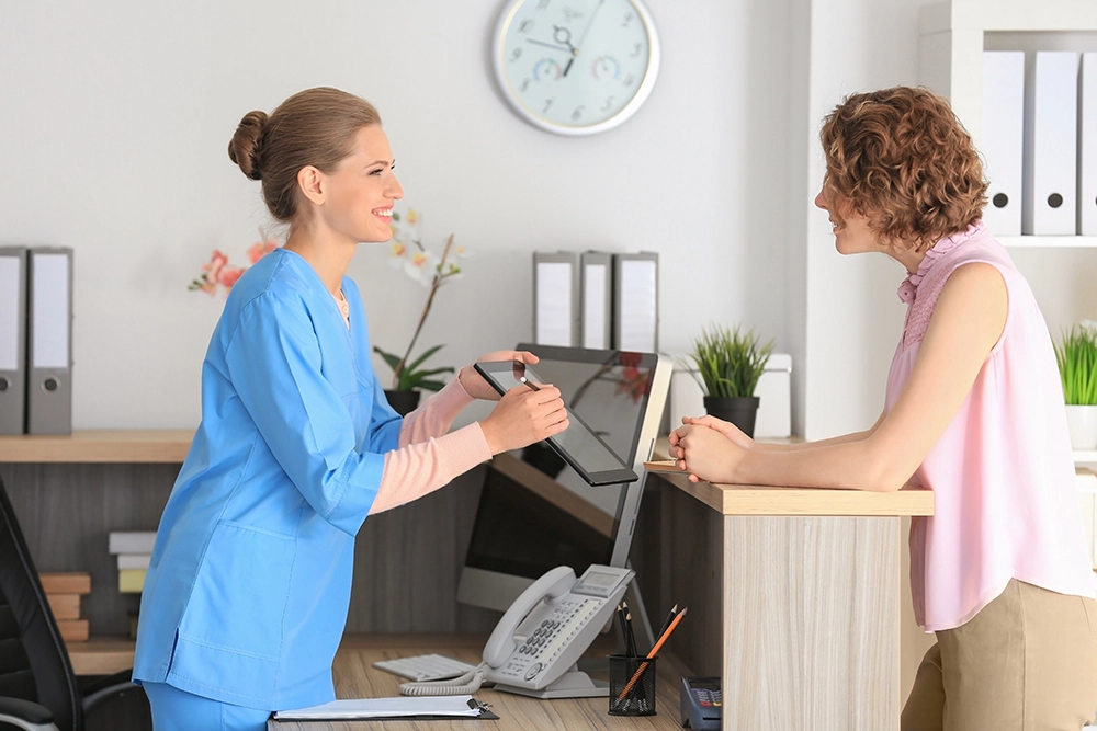 A nurse checking a patient into a medical facility at the front desk.