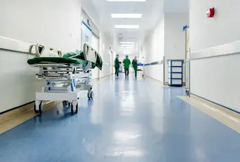 Hallway in a hospital with a shiny blue floor and nurses walking